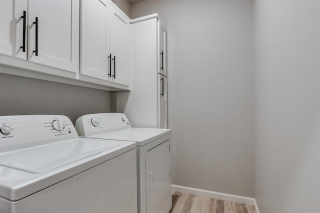 laundry room featuring washing machine and clothes dryer, cabinets, and light hardwood / wood-style floors