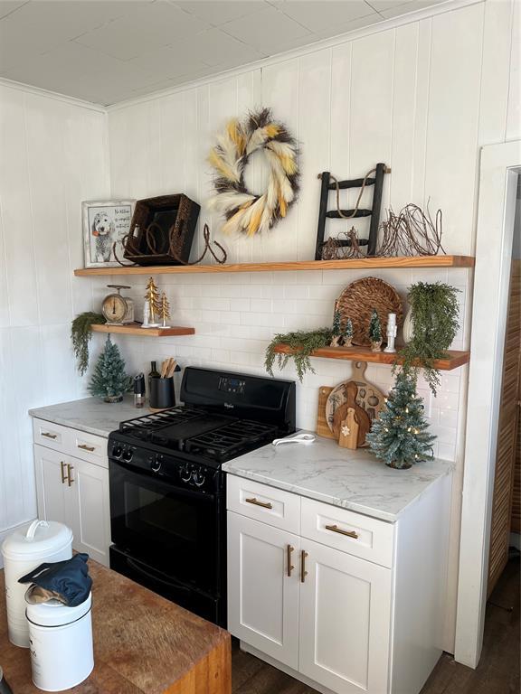 kitchen with black gas range, white cabinetry, tasteful backsplash, and light stone countertops