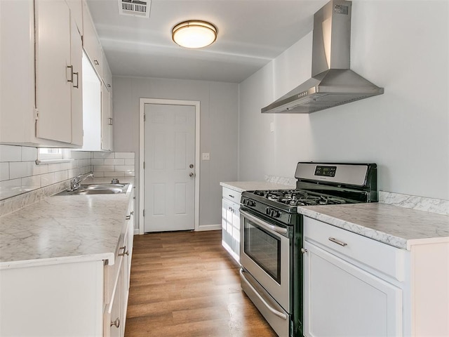 kitchen with stainless steel range with gas cooktop, wall chimney range hood, sink, light hardwood / wood-style floors, and white cabinetry