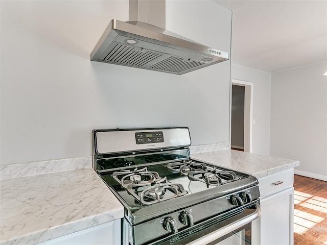 kitchen featuring wall chimney range hood, wood-type flooring, white cabinetry, and range with gas stovetop