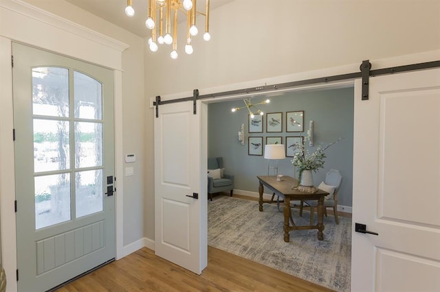 doorway to outside featuring baseboards, a barn door, a chandelier, and wood finished floors