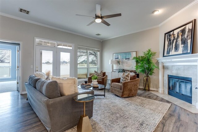 living room featuring crown molding, ceiling fan, wood-type flooring, and a tile fireplace