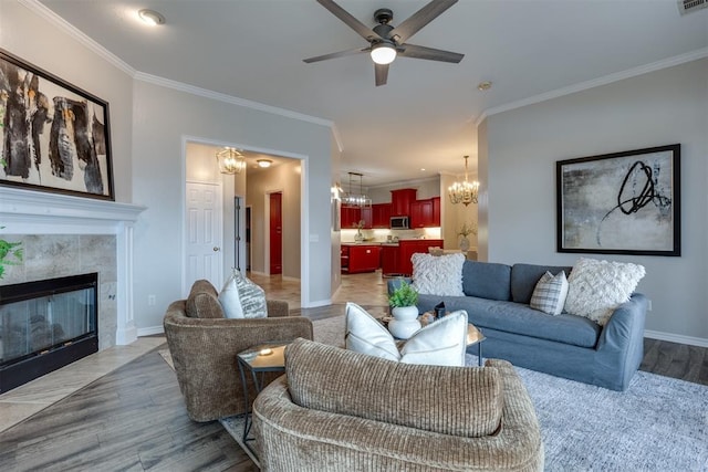 living room featuring a tiled fireplace, ornamental molding, ceiling fan with notable chandelier, and light hardwood / wood-style floors