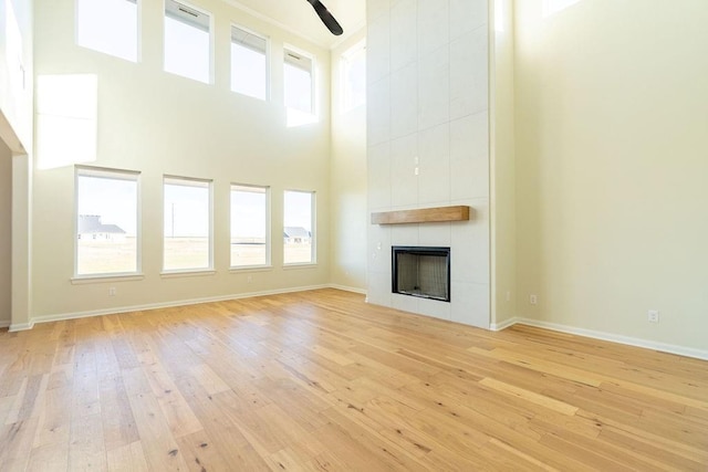 unfurnished living room with a tile fireplace, plenty of natural light, a towering ceiling, and light wood-type flooring