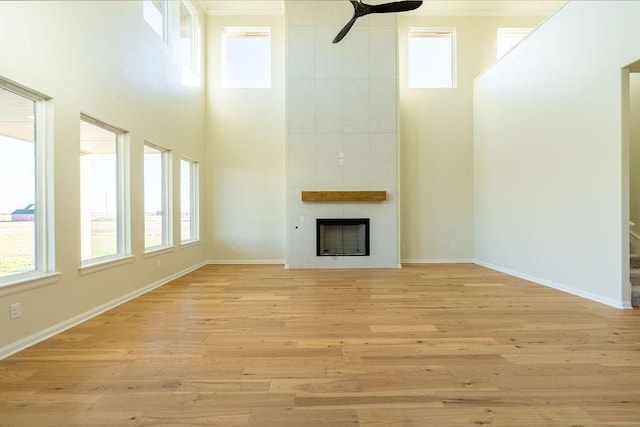 unfurnished living room featuring ceiling fan, light wood-type flooring, a high ceiling, and a tile fireplace