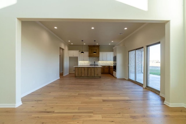 kitchen with ornamental molding, a center island with sink, hanging light fixtures, and light wood-type flooring