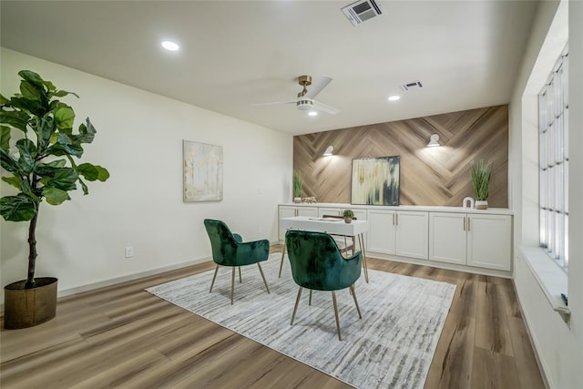 sitting room featuring hardwood / wood-style flooring, ceiling fan, and wooden walls