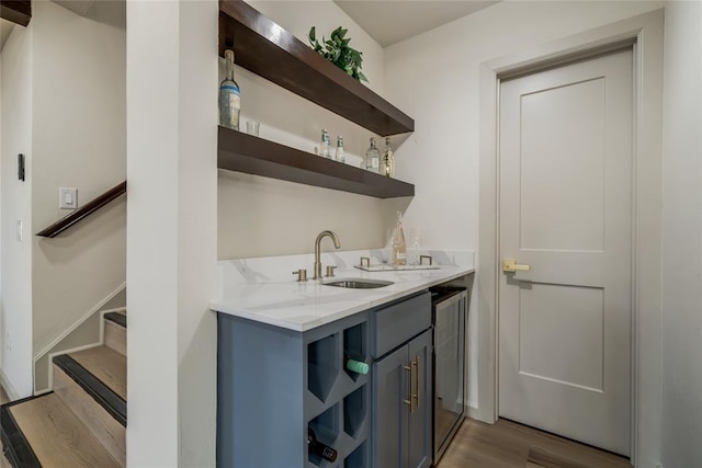 bar with gray cabinetry, light stone countertops, sink, and light hardwood / wood-style flooring