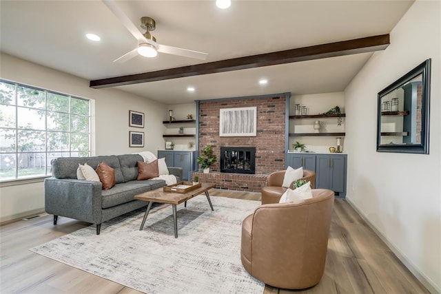 living room with beamed ceiling, ceiling fan, light wood-type flooring, and a fireplace