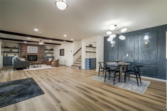 dining room with a brick fireplace, ceiling fan with notable chandelier, sink, beamed ceiling, and hardwood / wood-style floors