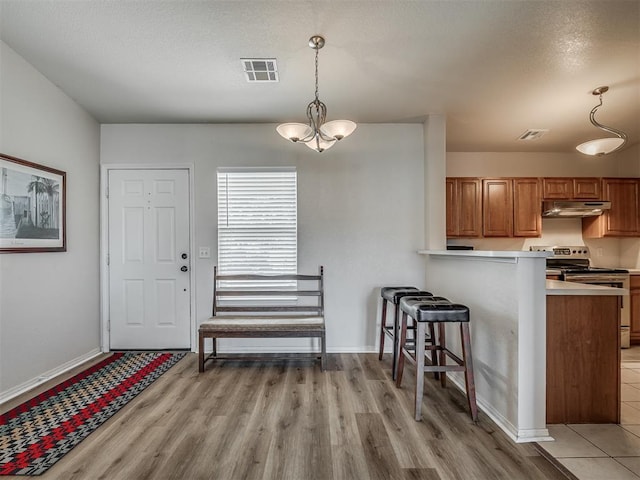 kitchen featuring kitchen peninsula, light hardwood / wood-style flooring, hanging light fixtures, a breakfast bar area, and stainless steel electric range