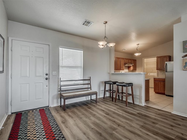 kitchen featuring kitchen peninsula, stainless steel fridge, washer / clothes dryer, decorative light fixtures, and light wood-type flooring