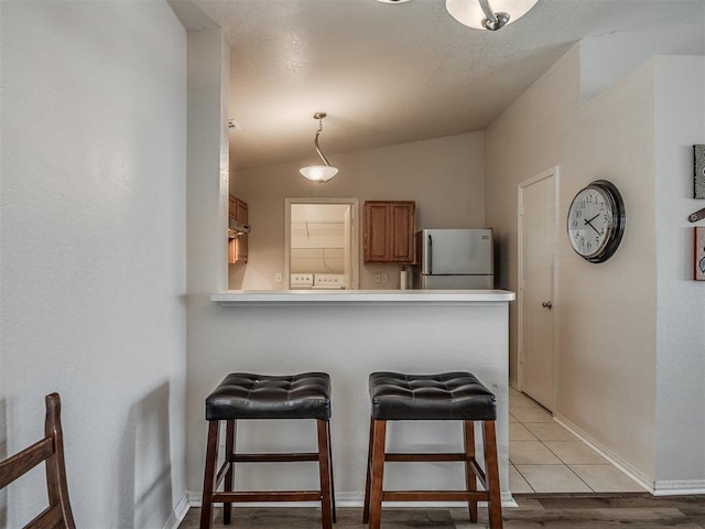 kitchen with stainless steel refrigerator, a breakfast bar, vaulted ceiling, and light hardwood / wood-style flooring