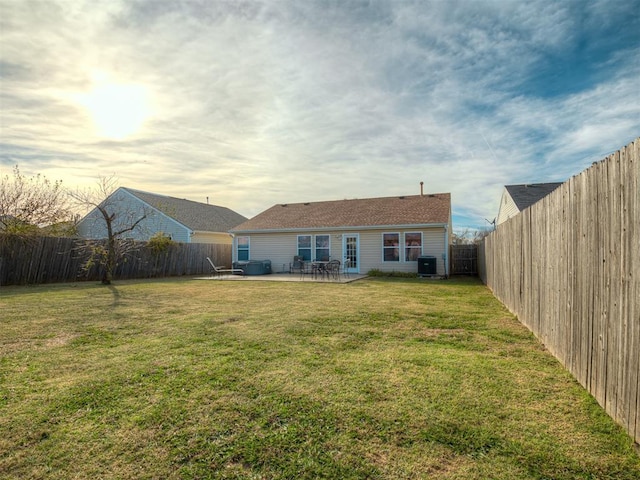 back house at dusk with a yard, central AC, and a patio area