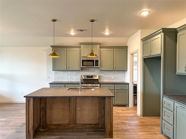 kitchen featuring sink, stainless steel appliances, light hardwood / wood-style flooring, decorative light fixtures, and a center island with sink