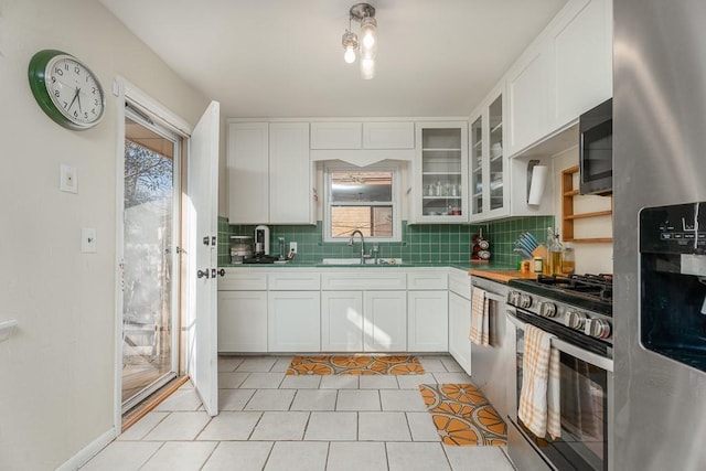 kitchen with sink, light tile patterned flooring, decorative backsplash, white cabinets, and appliances with stainless steel finishes