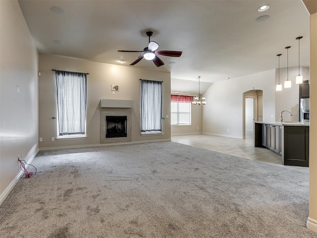 unfurnished living room featuring light carpet, ceiling fan with notable chandelier, and sink