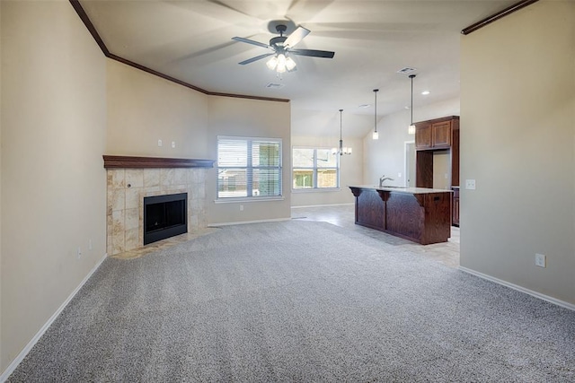 unfurnished living room with light carpet, ceiling fan with notable chandelier, ornamental molding, and a tiled fireplace