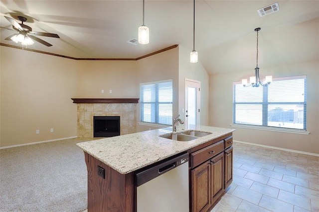 kitchen with a tile fireplace, ceiling fan with notable chandelier, sink, stainless steel dishwasher, and an island with sink