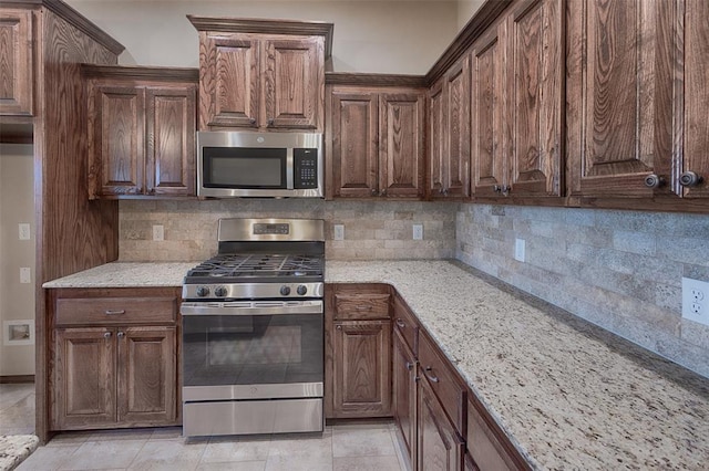 kitchen featuring tasteful backsplash, light stone countertops, light tile patterned floors, and appliances with stainless steel finishes