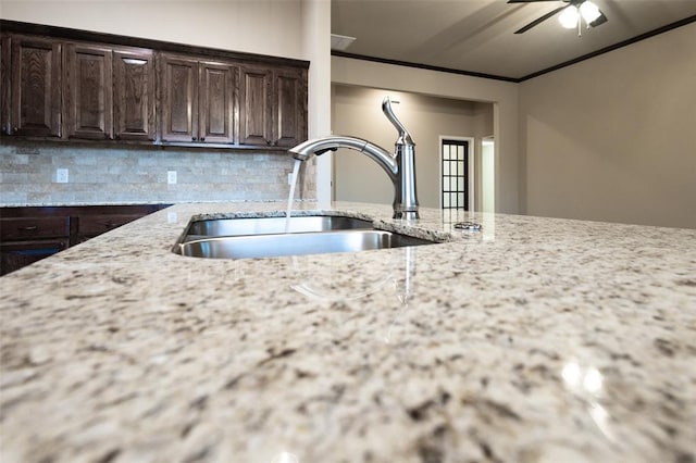 kitchen with light stone countertops, backsplash, dark brown cabinets, ceiling fan, and sink