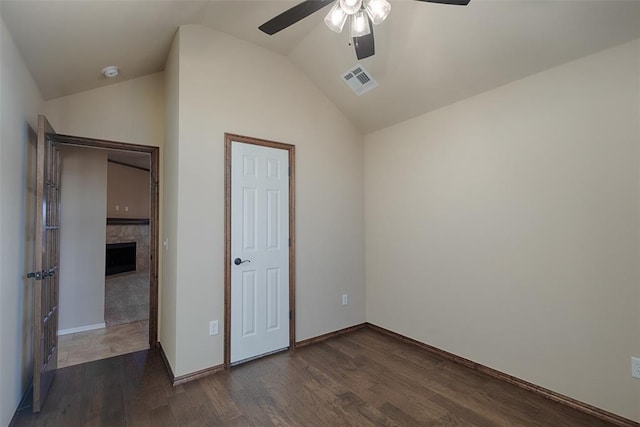 unfurnished bedroom with ceiling fan, dark hardwood / wood-style flooring, lofted ceiling, and a tile fireplace