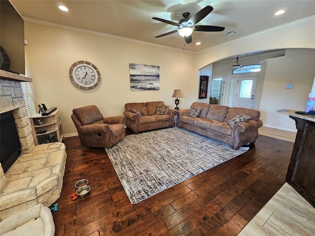 living room featuring dark wood-type flooring, a stone fireplace, ornamental molding, a wealth of natural light, and ceiling fan