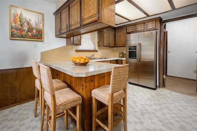 kitchen with stainless steel fridge with ice dispenser, a wainscoted wall, a peninsula, light countertops, and light floors