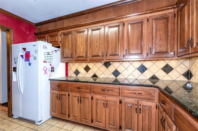 kitchen featuring white fridge with ice dispenser, dark stone countertops, crown molding, light tile patterned flooring, and backsplash