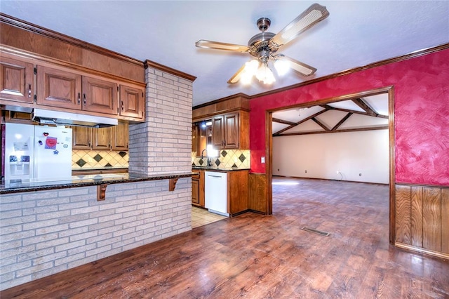 kitchen featuring white appliances, hardwood / wood-style floors, decorative backsplash, dark stone counters, and crown molding