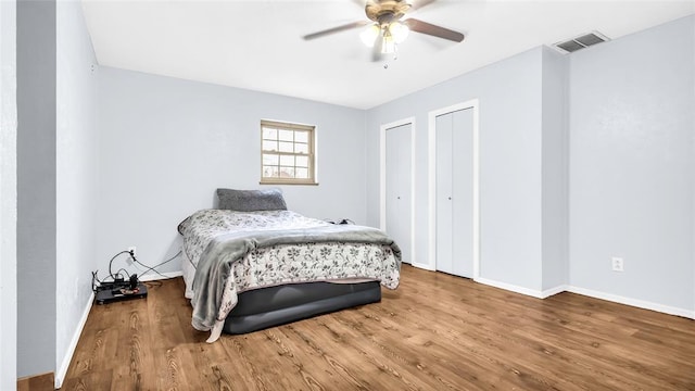 bedroom featuring two closets, hardwood / wood-style flooring, and ceiling fan