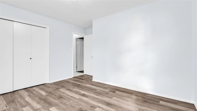 unfurnished bedroom with a closet, baseboards, and light wood finished floors