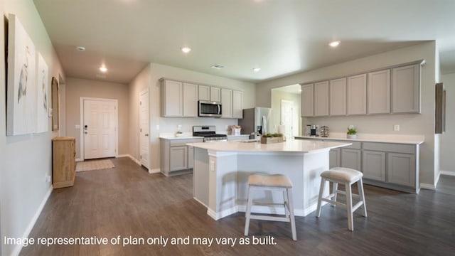 kitchen with stainless steel appliances, gray cabinets, light countertops, an island with sink, and a kitchen breakfast bar