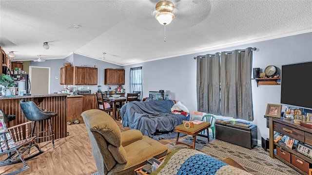 living room with ceiling fan, light wood-type flooring, crown molding, and vaulted ceiling