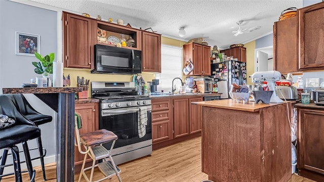 kitchen featuring sink, light wood-type flooring, a textured ceiling, black appliances, and ornamental molding