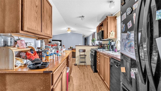 kitchen featuring black appliances, sink, light hardwood / wood-style flooring, vaulted ceiling, and ceiling fan