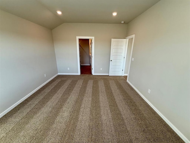 unfurnished bedroom featuring a closet, a walk in closet, lofted ceiling, and dark carpet