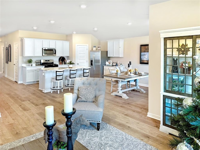 kitchen with light hardwood / wood-style floors, white cabinetry, appliances with stainless steel finishes, and an island with sink