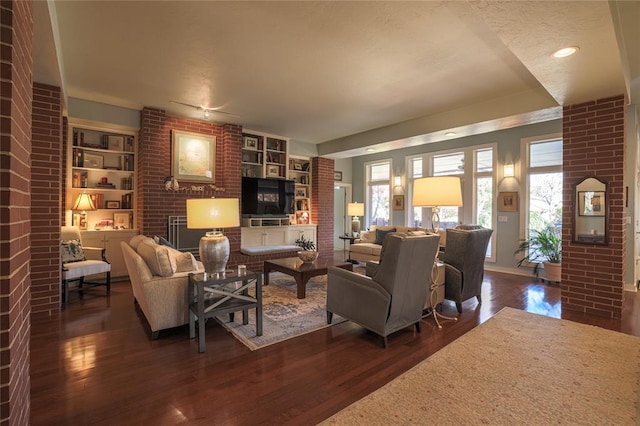 living room featuring dark hardwood / wood-style floors, built in shelves, and a brick fireplace