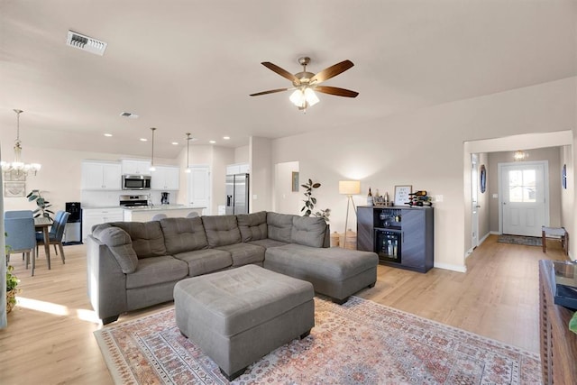 living room featuring ceiling fan with notable chandelier and light wood-type flooring