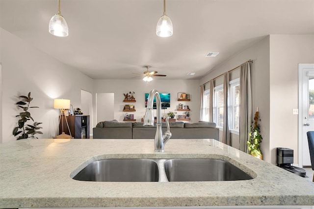 kitchen featuring light stone countertops, ceiling fan, hanging light fixtures, and sink