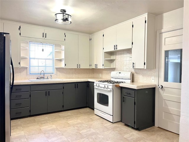 kitchen featuring stainless steel fridge, tasteful backsplash, white gas range, gray cabinetry, and sink