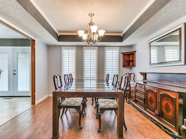 dining area with a tray ceiling, french doors, ornamental molding, and an inviting chandelier