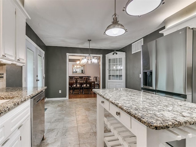 kitchen featuring a kitchen island, light stone counters, white cabinetry, stainless steel appliances, and a chandelier