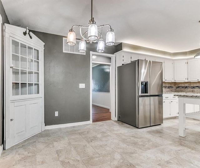 kitchen featuring white cabinets, stainless steel fridge, light stone countertops, tasteful backsplash, and decorative light fixtures