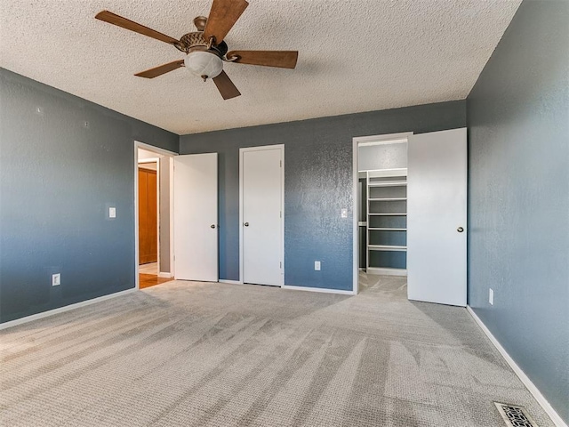 unfurnished bedroom featuring a textured ceiling, ceiling fan, a spacious closet, and light carpet