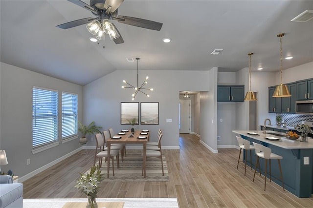 dining space featuring ceiling fan with notable chandelier, light wood-type flooring, and vaulted ceiling