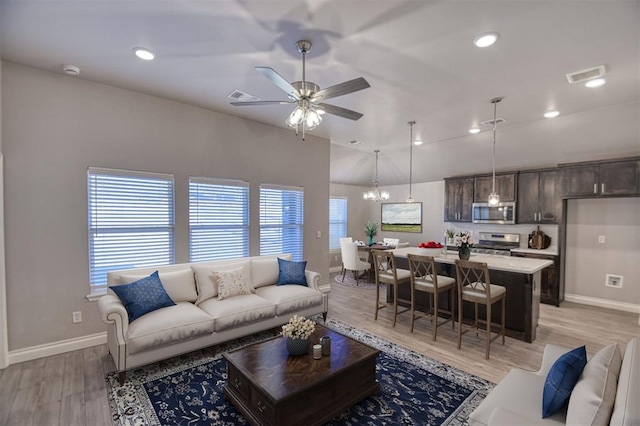 living room with ceiling fan with notable chandelier and light hardwood / wood-style floors