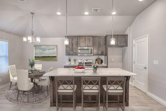 kitchen with vaulted ceiling, appliances with stainless steel finishes, decorative light fixtures, an island with sink, and a kitchen bar