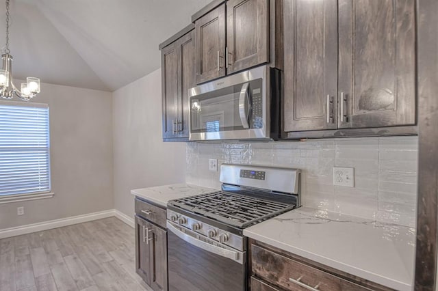 kitchen with dark brown cabinetry, lofted ceiling, hanging light fixtures, appliances with stainless steel finishes, and light stone countertops